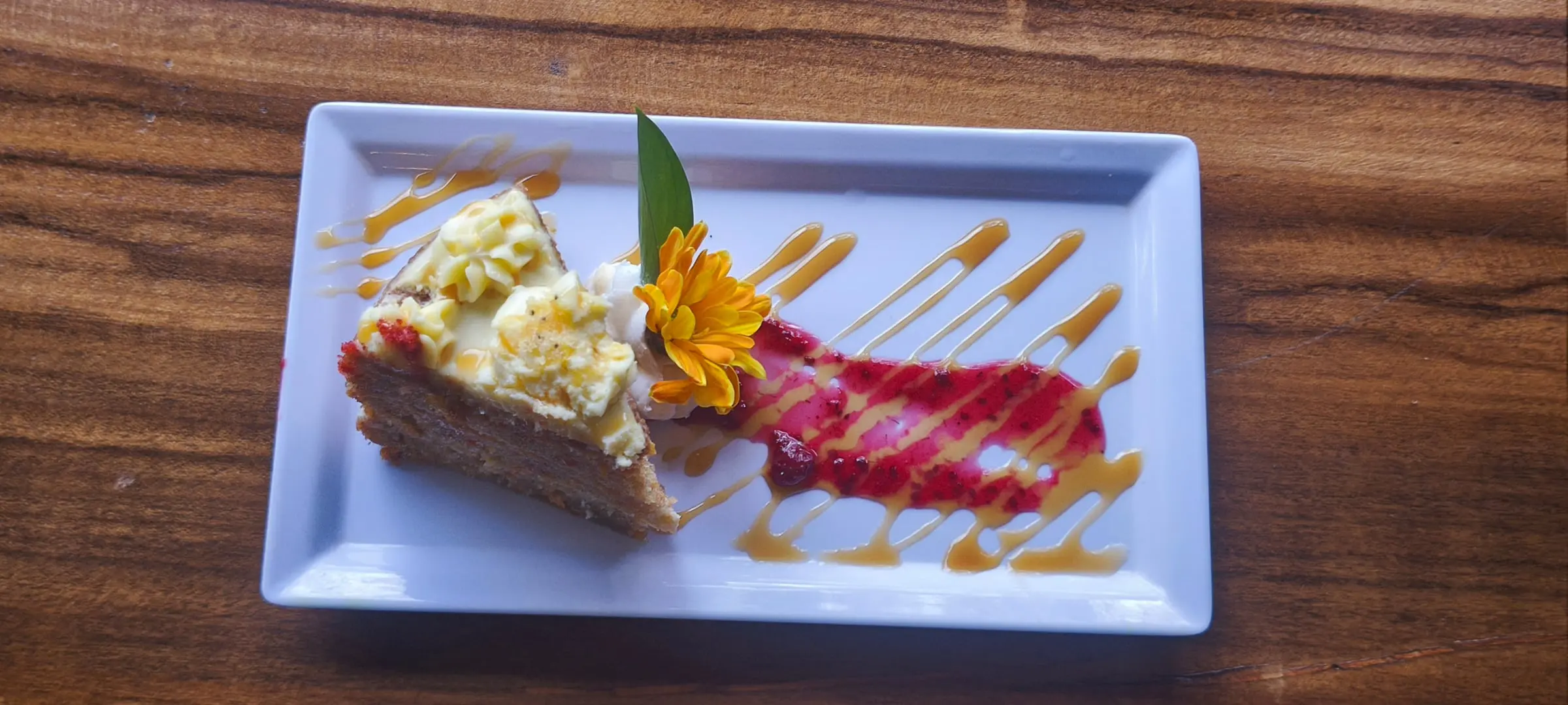 Torta con crema, flor comestible y salsa de frutos rojos